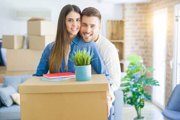 Beautiful young couple moving to a new house, smiling happy holding cardboard boxes at new apartment - Fotó, kép