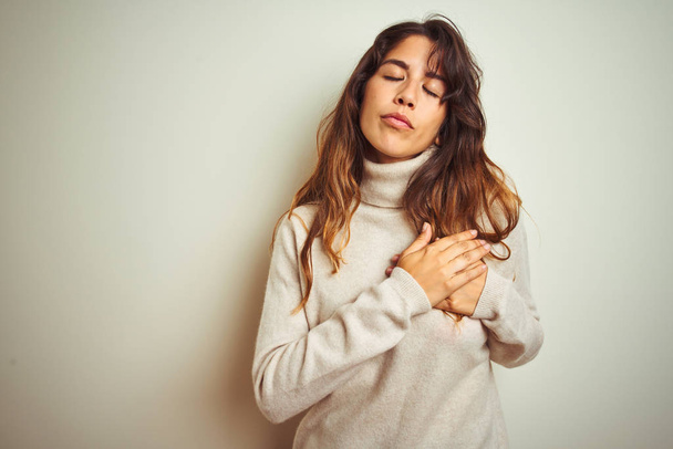 Young beautiful woman wearing winter sweater standing over white isolated background smiling with hands on chest with closed eyes and grateful gesture on face. Health concept. - Фото, зображення