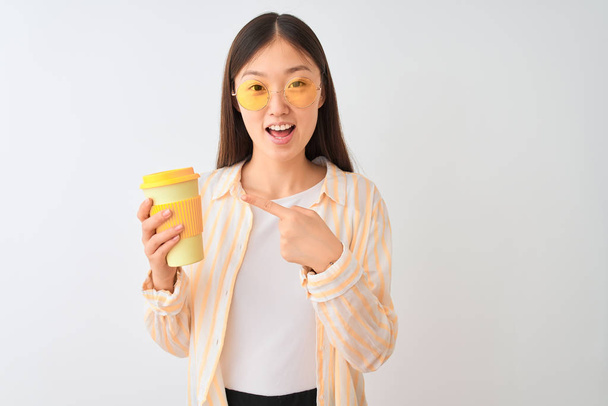 Young chinese woman wearing glasses drinking coffe over isolated white background very happy pointing with hand and finger - Fotografie, Obrázek