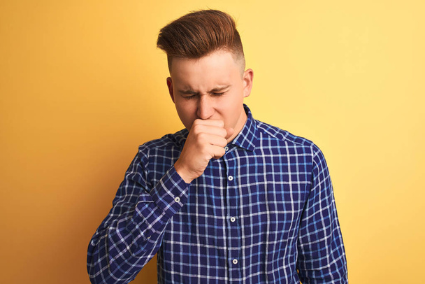 Young handsome man wearing casual shirt standing over isolated yellow background feeling unwell and coughing as symptom for cold or bronchitis. Healthcare concept. - Fotó, kép