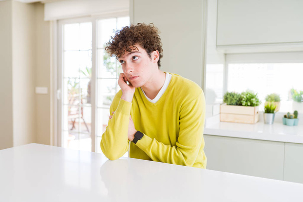 Fiatal jóképű férfi visel sárga pulóvert otthon gondolkodás látszó fáradt és unatkozott a depresszió problémák keresztbe fegyverek. - Fotó, kép