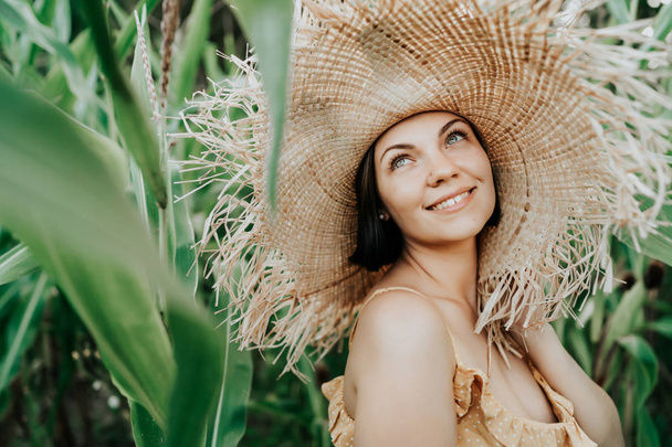Portrait of young beautiful woman in big trendy straw hat posing and smiling in tropical jungle. Happiness, travel, vacation concept - Фото, зображення