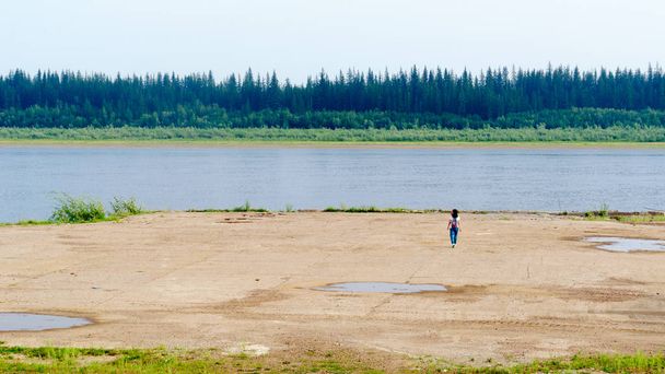 Touristen mit Rucksack, die zu den Betonklippen laufen, ist ein Anblick am Ufer der alten Seebrücke nördlich des Flusses vilyui mit Fichtenwäldern und Tundra von Jakutien auf der anderen Seite. - Foto, Bild