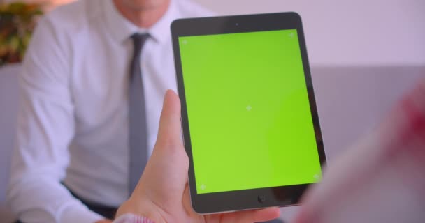 Closeup portrait of businessman talking to client holding tablet with green chroma key screen in office - Materiał filmowy, wideo