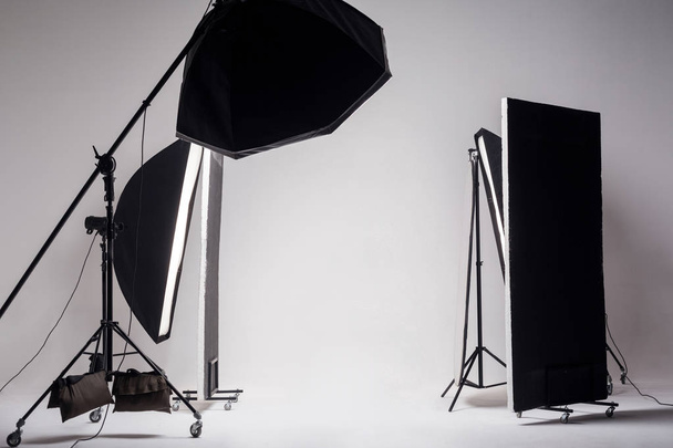 Professional photo studio with light setup and octagon softbox on boom with strip softbox and reflector on light gray background  - Foto, afbeelding