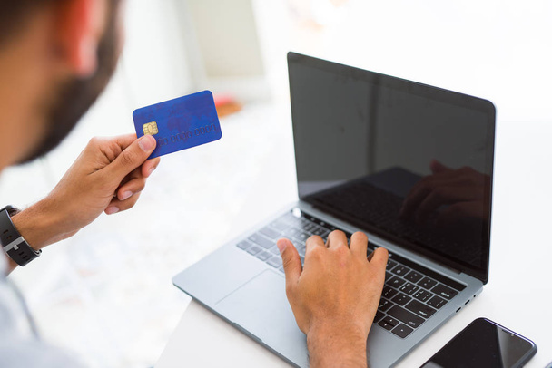 Mies käyttää luottokorttia maksuvälineenä tehdessään ostoksia verkossa
 - Valokuva, kuva