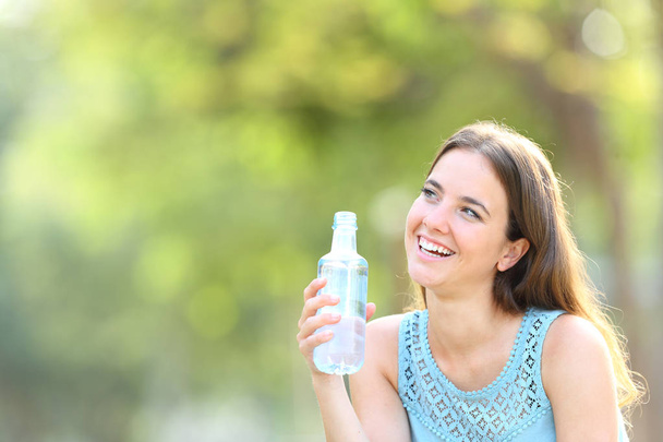 Счастливая женщина, держащая бутылку с водой, смотрит в сторону
 - Фото, изображение