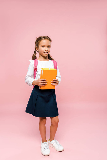 happy kid holding books while standing with backpack on pink  - Zdjęcie, obraz