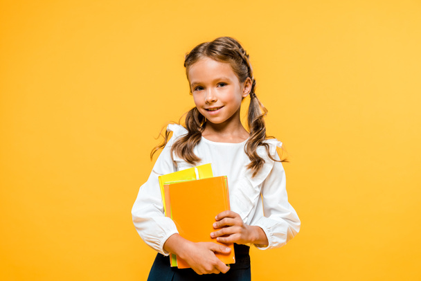 glückliches Kind hält Bücher in der Hand und lächelt isoliert auf orange  - Foto, Bild