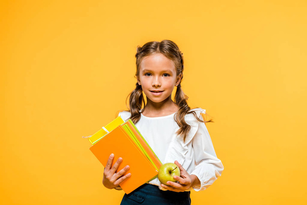 happy kid holding books and tasty apple isolated on orange  - Photo, image