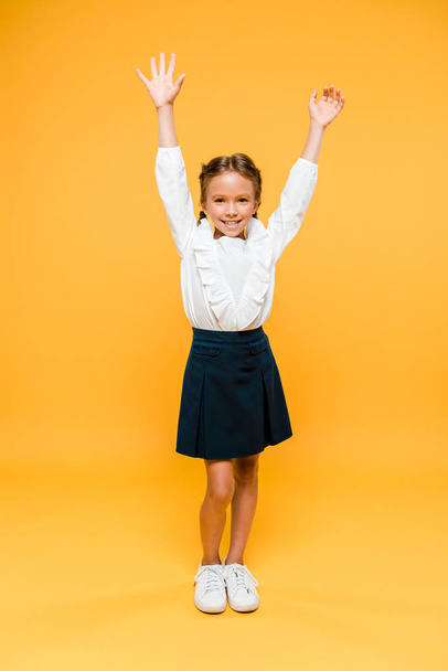 happy schoolgirl standing with hands above head on orange  - Valokuva, kuva