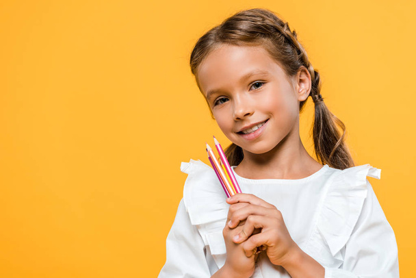 cheerful schoolgirl holding color pencils isolated on orange  - Photo, image