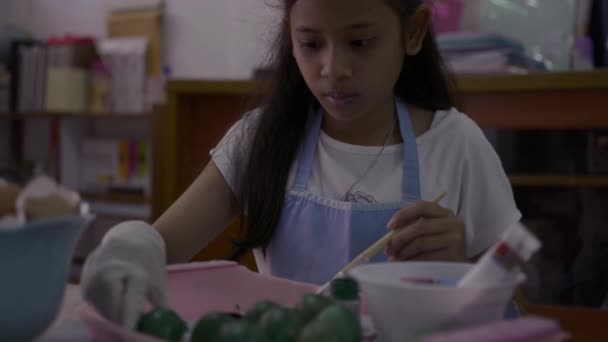 Asiática linda chica está haciendo manualidades de cáscaras de huevo en el escritorio, Chica joven está coloreando cáscaras de huevo en casa para su tarea, concepto de educación
. - Imágenes, Vídeo