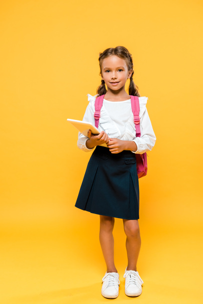 cheerful schoolchild with pink backpack holding book on orange  - Photo, Image