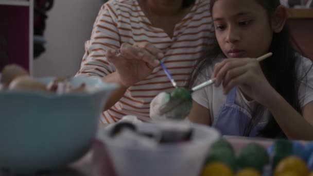 Menina asiática e sua mãe estão fazendo artesanato a partir das cascas de ovos, mãe ajudando sua filha a pintar cascas de ovos juntos em casa, conceito de educação
. - Filmagem, Vídeo