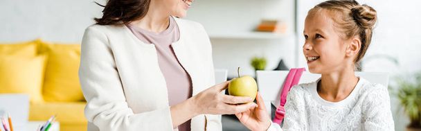 panoramic shot of happy mother giving apple to daughter  - Photo, Image