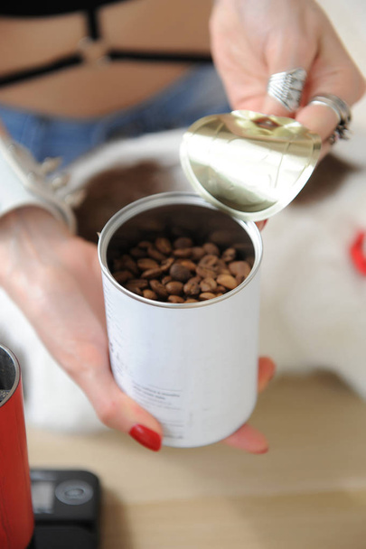 Barista girl opens tin can with coffee close up. Freshly roasted. Red manual grinder. White cat - Photo, Image