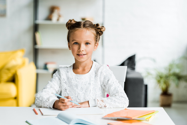 щаслива дитина тримає кольоровий олівець, сидячи біля столу
  - Фото, зображення