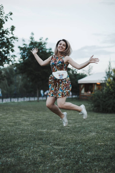 Young happy woman with beige belt cotton bag on it jumping at the street on grass.  - Fotografie, Obrázek