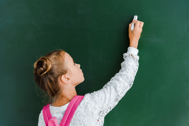 schoolchild holding chalk near chalkboard on green  - Fotó, kép