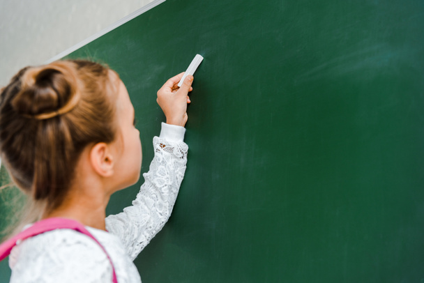 selective focus of schoolgirl holding chalk near green chalkboard  - Φωτογραφία, εικόνα