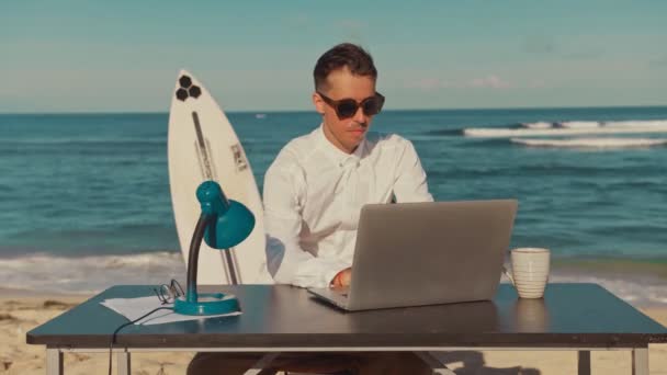 Jonge duizendjarige met laptop op tafel tegen op het strand blij om bericht te ontvangen - Video