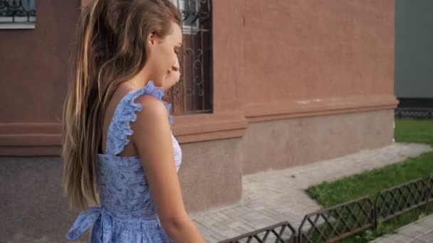 karcsú európai modell divatos kék ruhában sétál utca mentén - Felvétel, videó