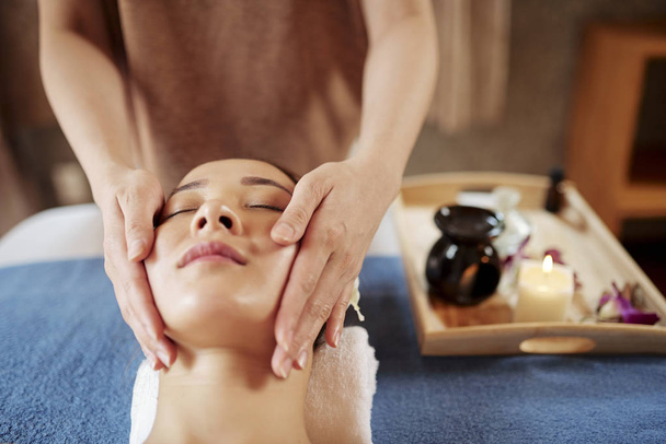 Pretty young Asian woman getting face spa treatment with natural oils in spa salon - Photo, Image