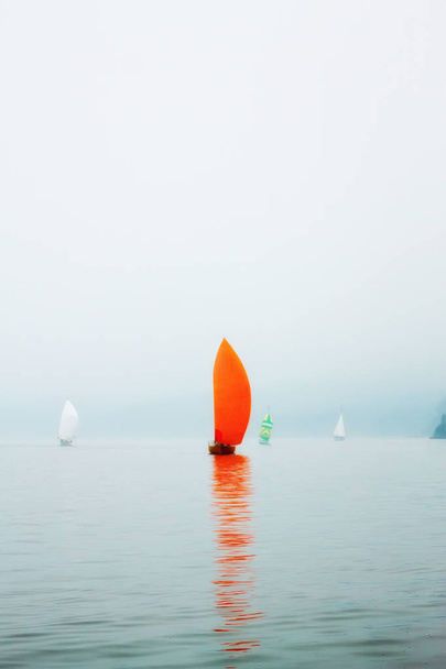 Yacht regatta with an orange sail in a foggy morning floats on the sea - Foto, Imagem