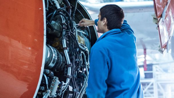 Mecânico de manutenção de aeronaves inspeciona e sintoniza o motor de avião em um hangar
. - Foto, Imagem