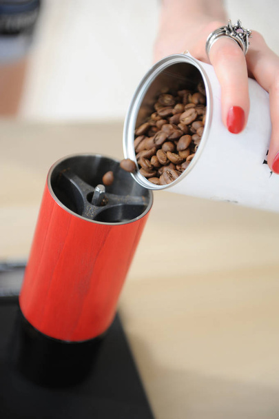 Barista fille verse des grains de café d'une boîte blanche dans un moulin à café manuel rouge gros plan
 - Photo, image