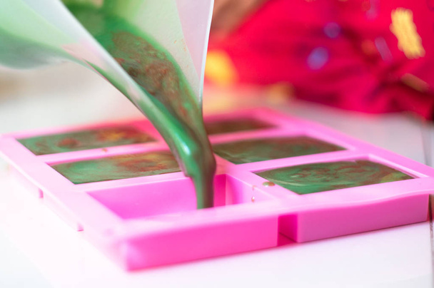 Versare sapone verde miscela colorata con turbinii rossi da una nave con muso in uno stampo rosa per fare le saponette fatte a mano fatte in casa finale
 - Foto, immagini