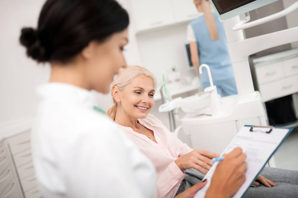 Woman helping her dentist writing information about her. - 写真・画像