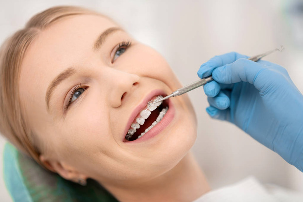 Ο ασθενής διορθώνει τα ορθοδοντικά σιδεράκια της στην οδοντιατρική κλινική. - Φωτογραφία, εικόνα