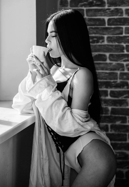 Attractive female lingerie relaxing at home. Passionate mysterious lover. Perfect coffee time. But first coffee. Enjoying morning sunlight. Sensual girl sexy breasts drinking coffee near windowsill - Photo, image