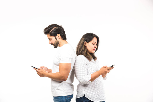 スマートフォン/携帯電話を使用してインドのカップルは、白い背景の上に孤立して立っています - 写真・画像