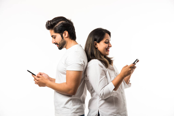 Indian couple using smartphone / mobile handset, standing isolated over white background - Fotoğraf, Görsel