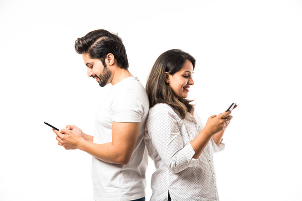 Indian couple using smartphone / mobile handset, standing isolated over white background - Photo, image
