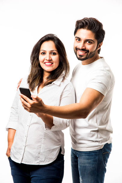Indian couple using smartphone / mobile handset, standing isolated over white background - Foto, Imagen