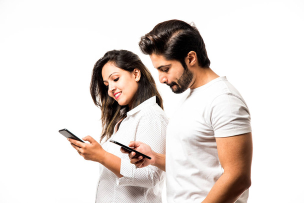 Indian couple using smartphone / mobile handset, standing isolated over white background - Valokuva, kuva