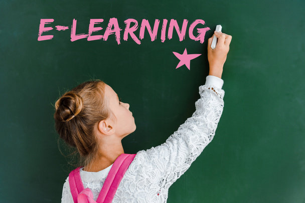schoolchild holding chalk near chalkboard with e-learning lettering on green  - Φωτογραφία, εικόνα