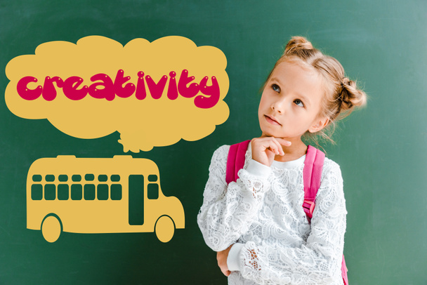 pensive kid standing with backpack near chalkboard with school bus and creativity lettering on green  - Photo, Image