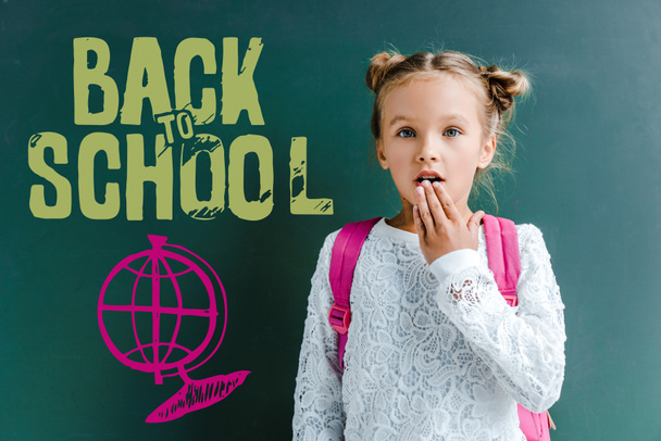 meglepett iskoláslány kiterjedő száj közelében Chalkboard vissza az iskolai leveleket zöld  - Fotó, kép
