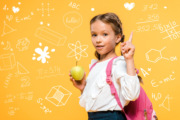 очаровательный школьник держит яблоко и указывает пальцем рядом с математическими формулами на оранжевый
  - Фото, изображение
