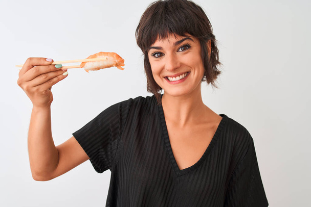 Beautiful woman eating salmon nigiri sushi using chopsticks over isolated white background with a happy face standing and smiling with a confident smile showing teeth - Photo, image