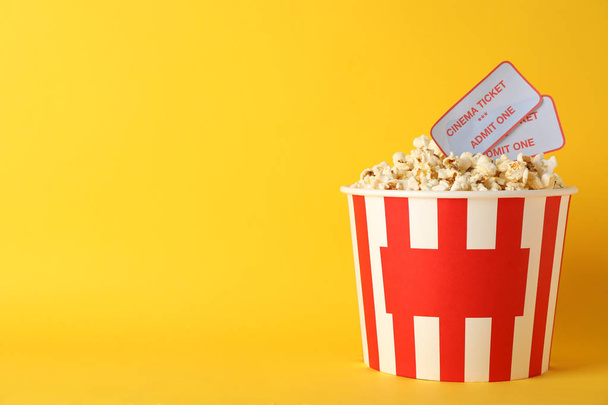 Striped bucket with popcorn and tickets on yellow background, co - Zdjęcie, obraz