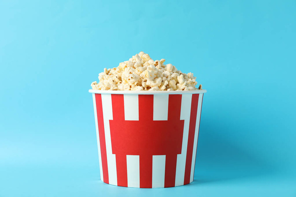 Striped bucket with popcorn on blue background, space for text - Фото, изображение