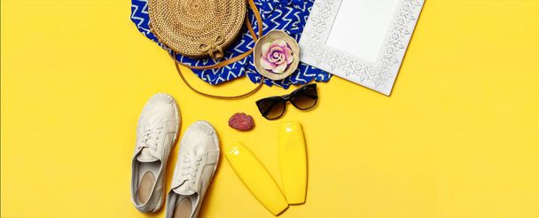 女性の夏のファッションの背景。黄色の背景に服やアクセサリー。青いドレス、丸いラタンバッグ、エスパドリーユの靴、サングラス、日焼け止め、木製の額縁。フラットレイトップビュー - 写真・画像
