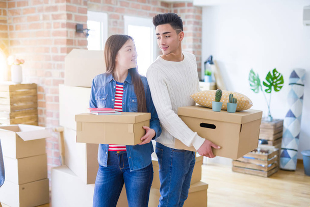 Красивая молодая азиатская пара выглядит счастливой, держа картонные коробки, улыбаясь взволнованный переезд в новый дом
 - Фото, изображение