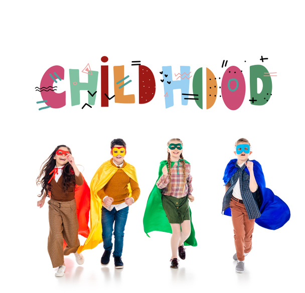 crianças felizes em trajes de super-herói e máscaras correndo perto de letras de infância em branco
 - Foto, Imagem